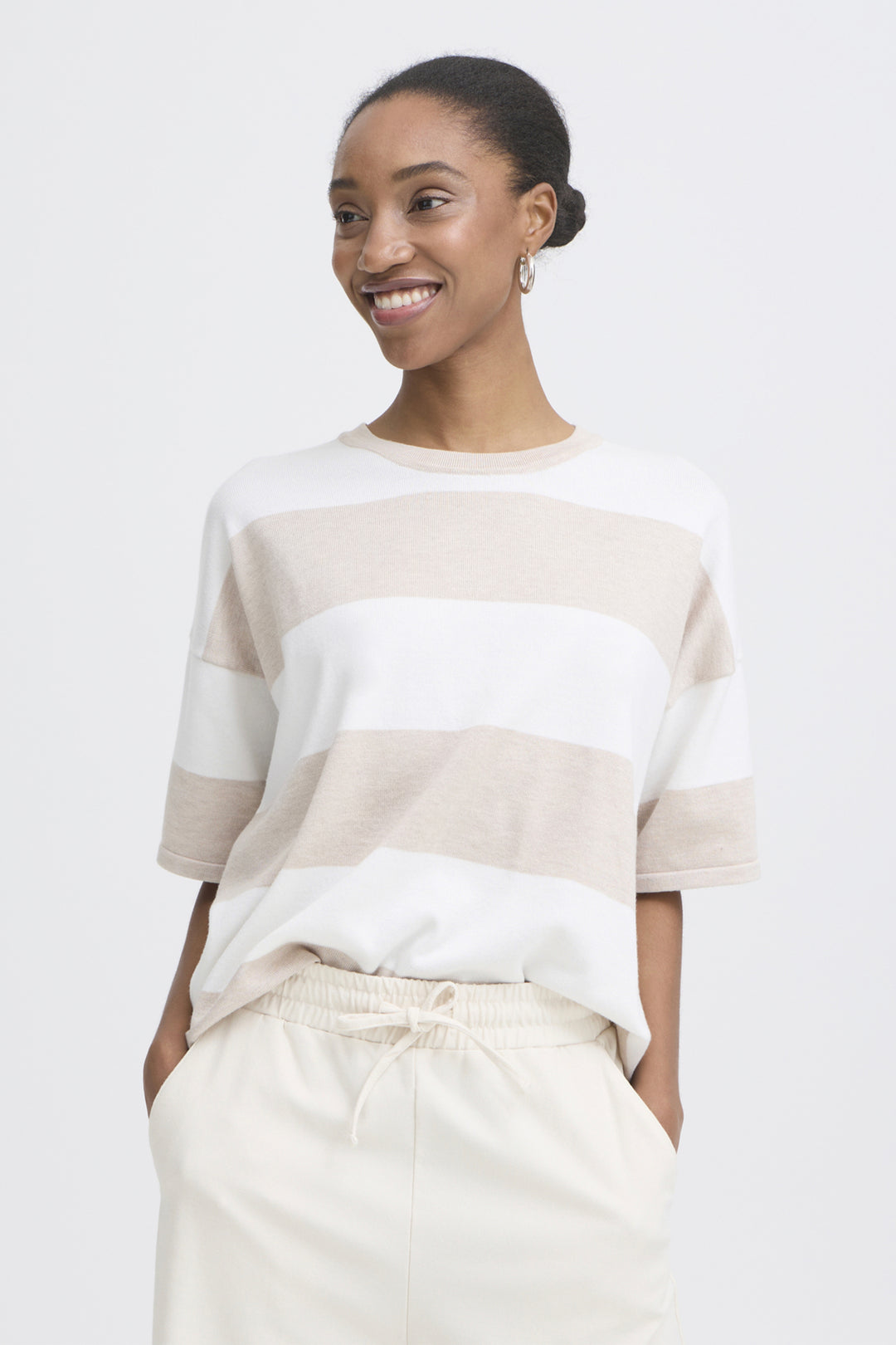 Woman wearing a white and beige striped sweater with beige pants on a white background