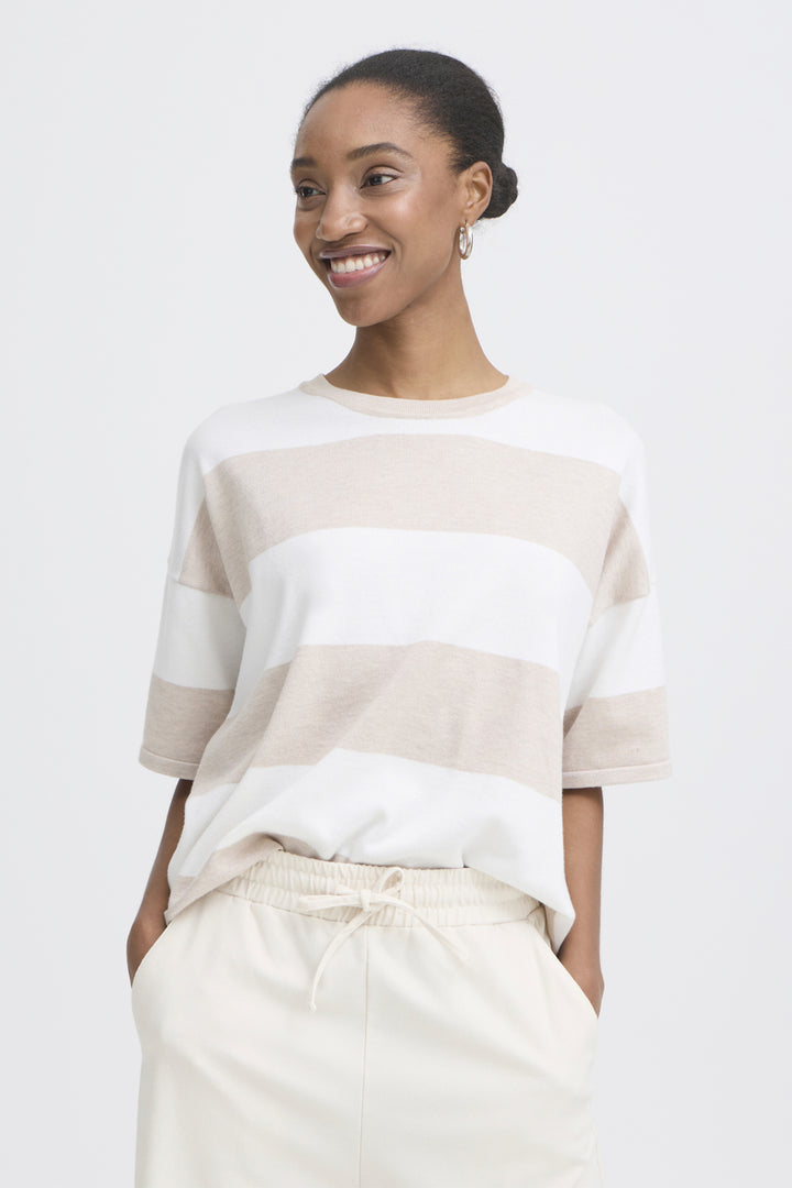 Woman wearing a white and beige striped sweater with beige pants on a white background