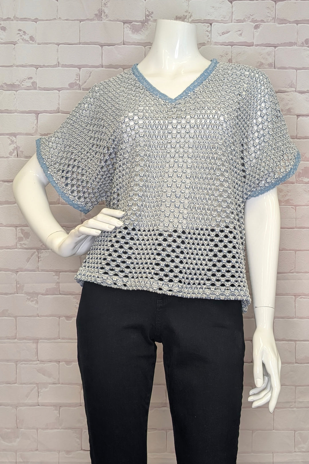 Mannequin wearing a silver chainmail crochet sweater top with blue trim against a gray brick wall.