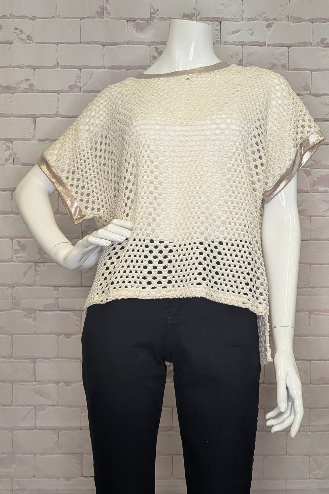 Mannequin wearing a beige crochet sweater top against a gray brick wall.