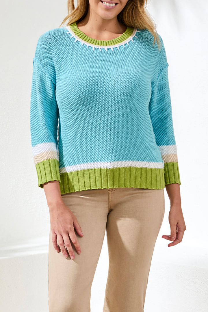 Woman wearing a blue cotton sweater with green accents on a white background