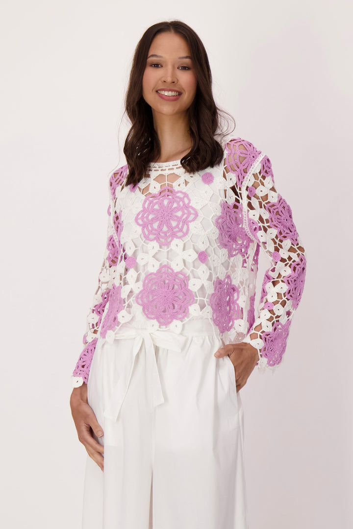 Woman wearing a floral crochet sweater top with a plain background
