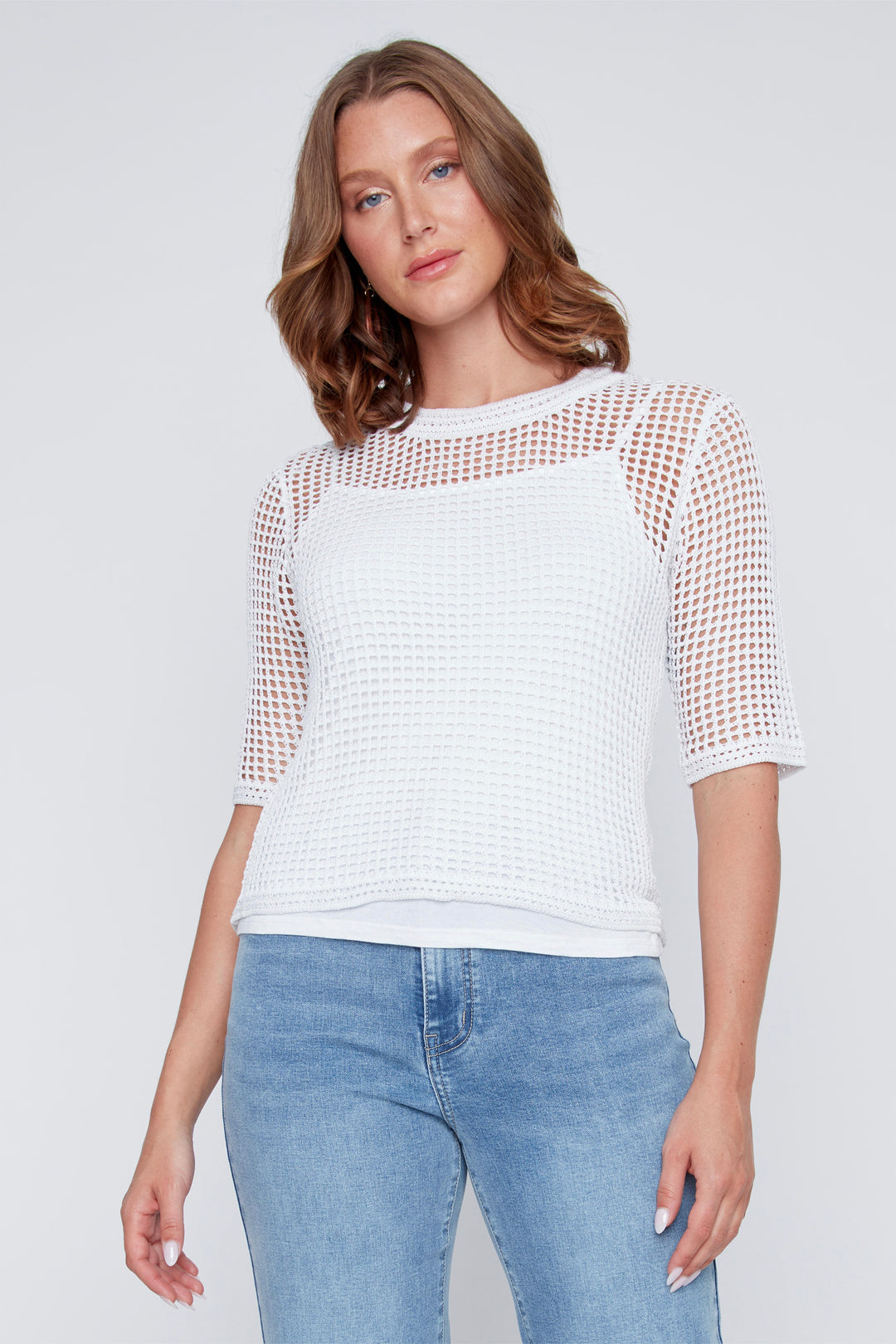 Woman wearing a white tank top with mesh sleeves cardigan top and blue jeans on a light gray background