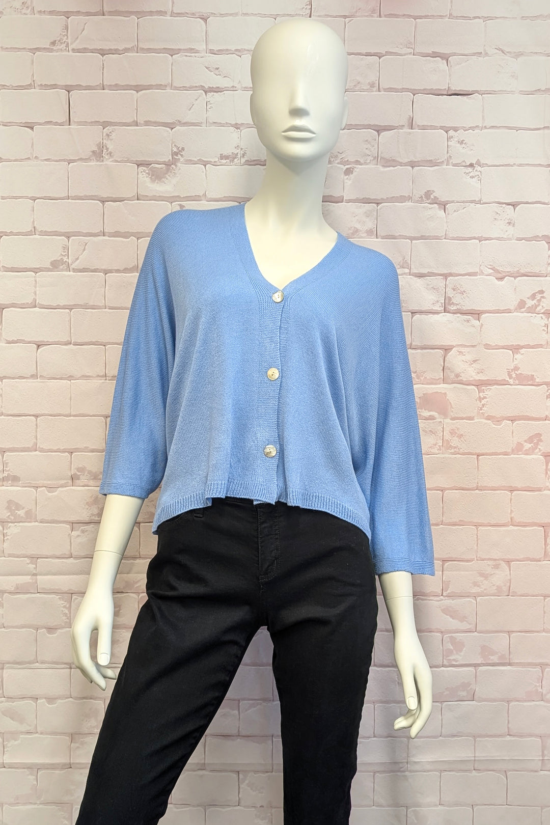 Mannequin wearing a light blue button cardigan and black pants against a brick wall.