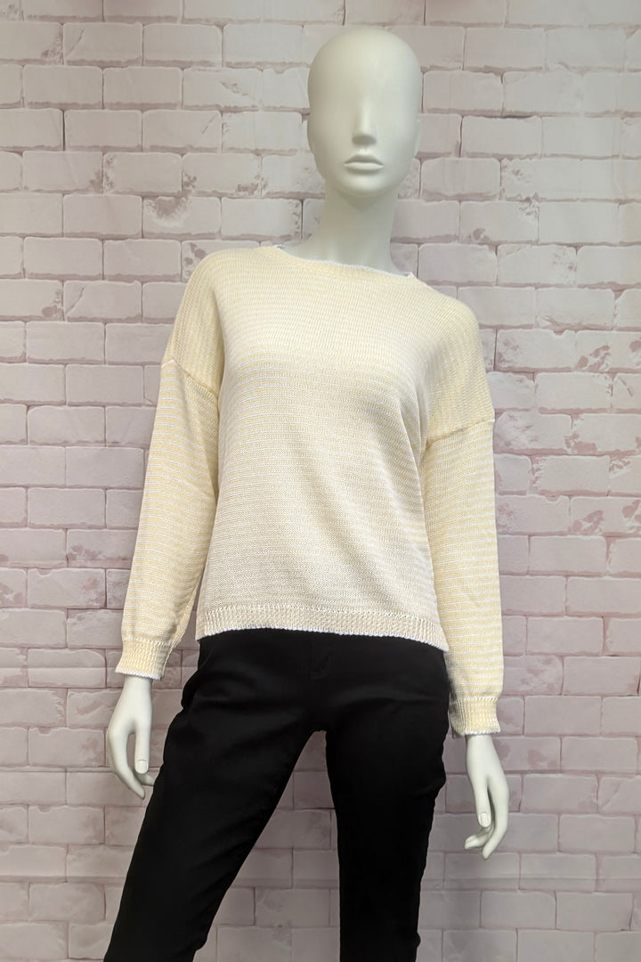 Mannequin wearing a beige light cotton sweater and black pants against a textured wall.