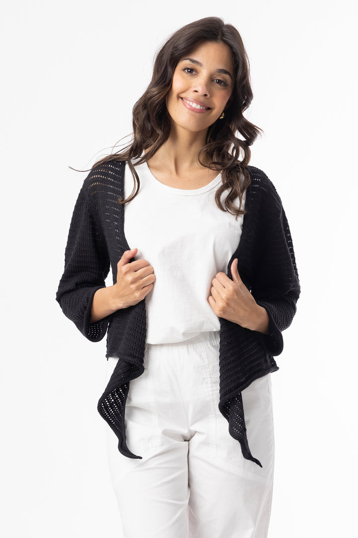 Woman wearing a black open cardigan over a white shirt and pants on a white background