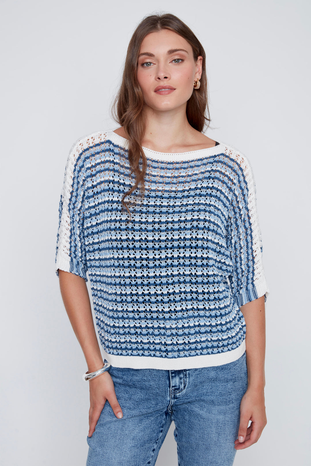 Woman wearing a blue and white patterned crochet sweater with jeans on a light gray background