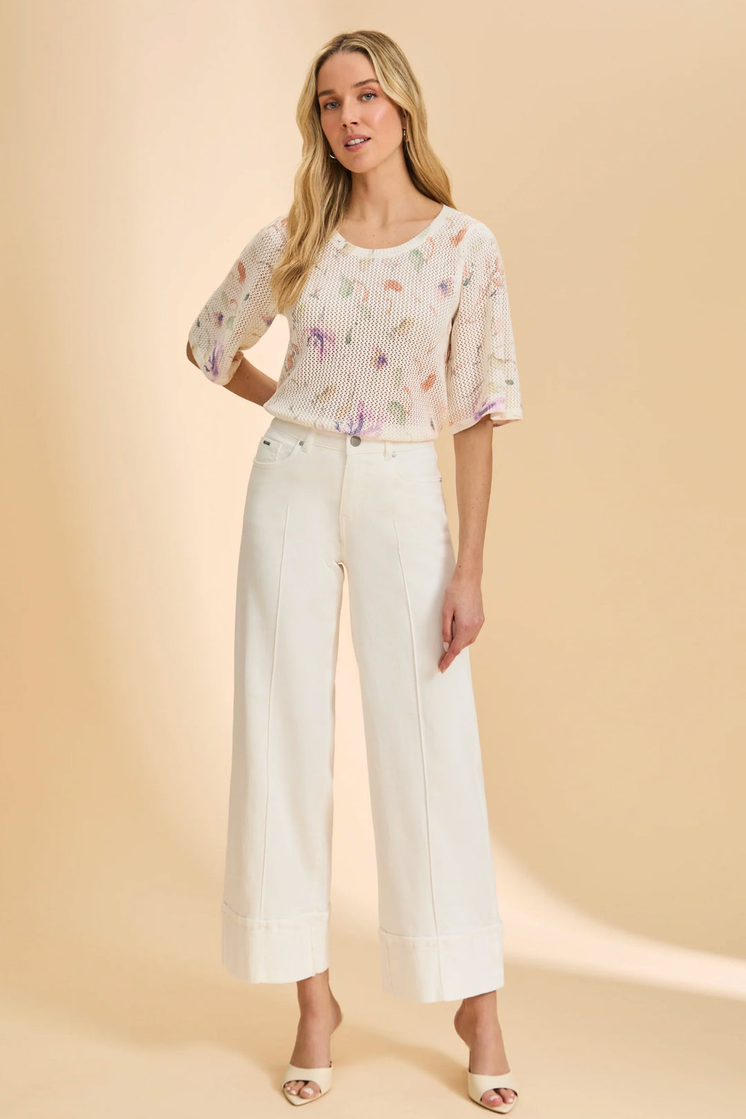 Woman wearing a floral blouse and white pants on a beige background