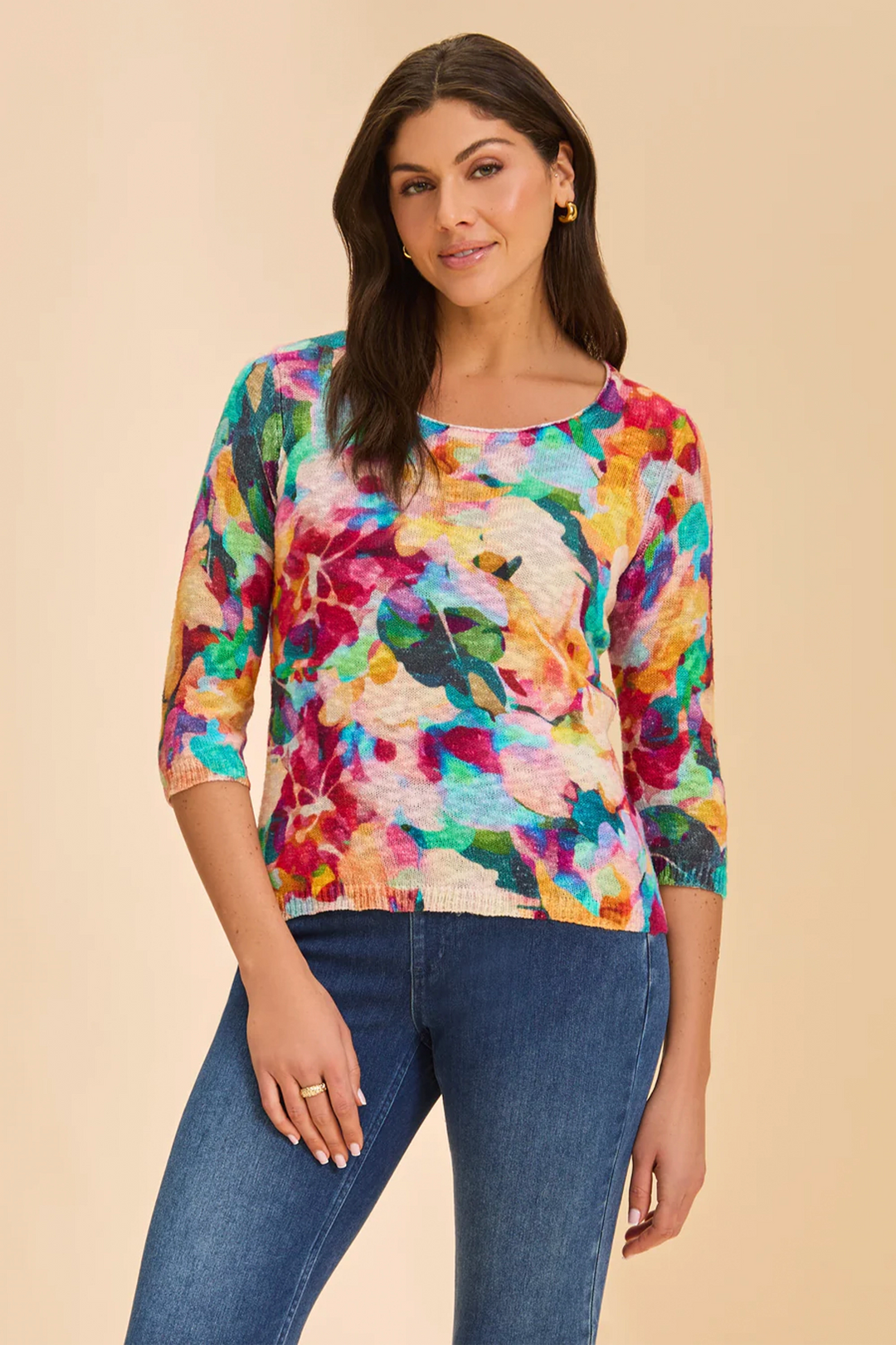 Woman wearing a colorful floral-patterned sweater and blue jeans on a beige background