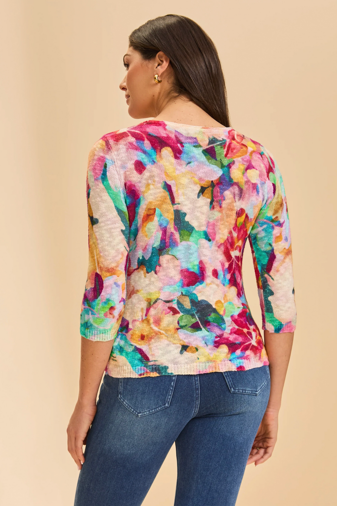 Woman wearing a colorful floral top and blue jeans on a beige background