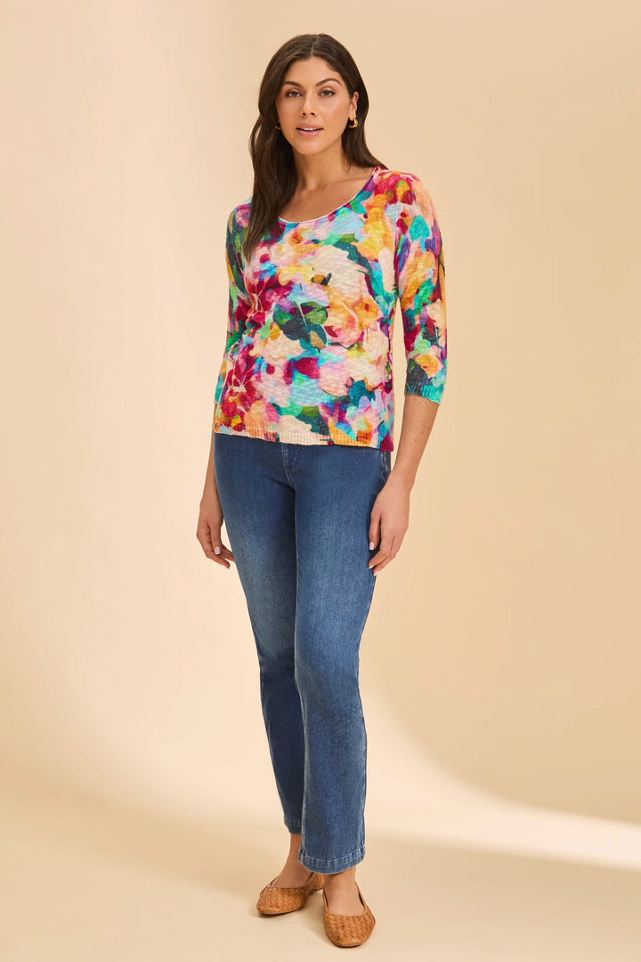 Woman wearing a colorful floral top and blue jeans on a beige background