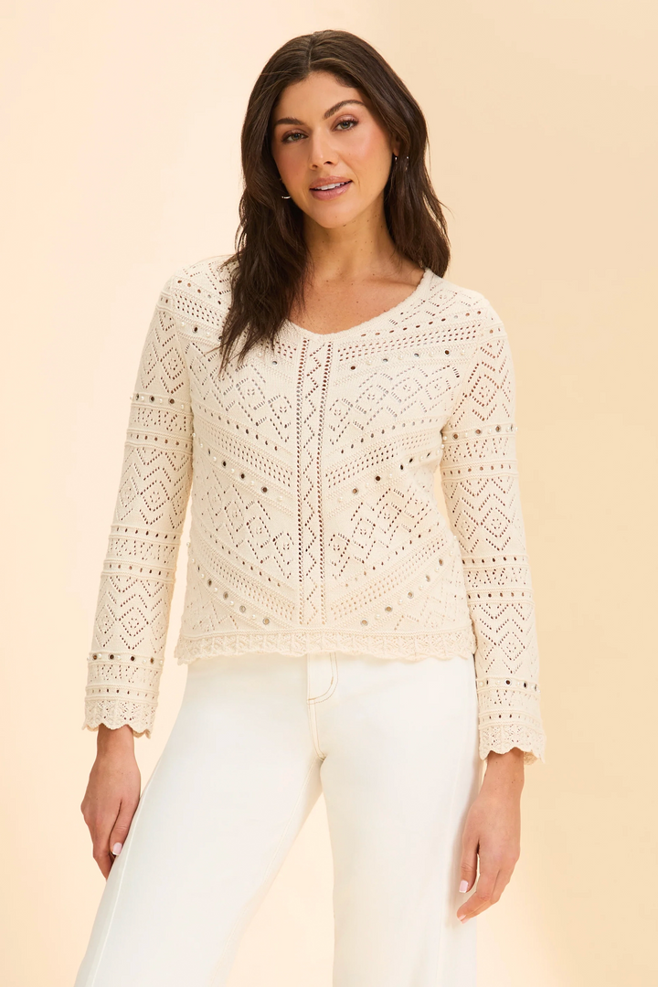 Woman wearing a cream lace top and white pants against a beige background