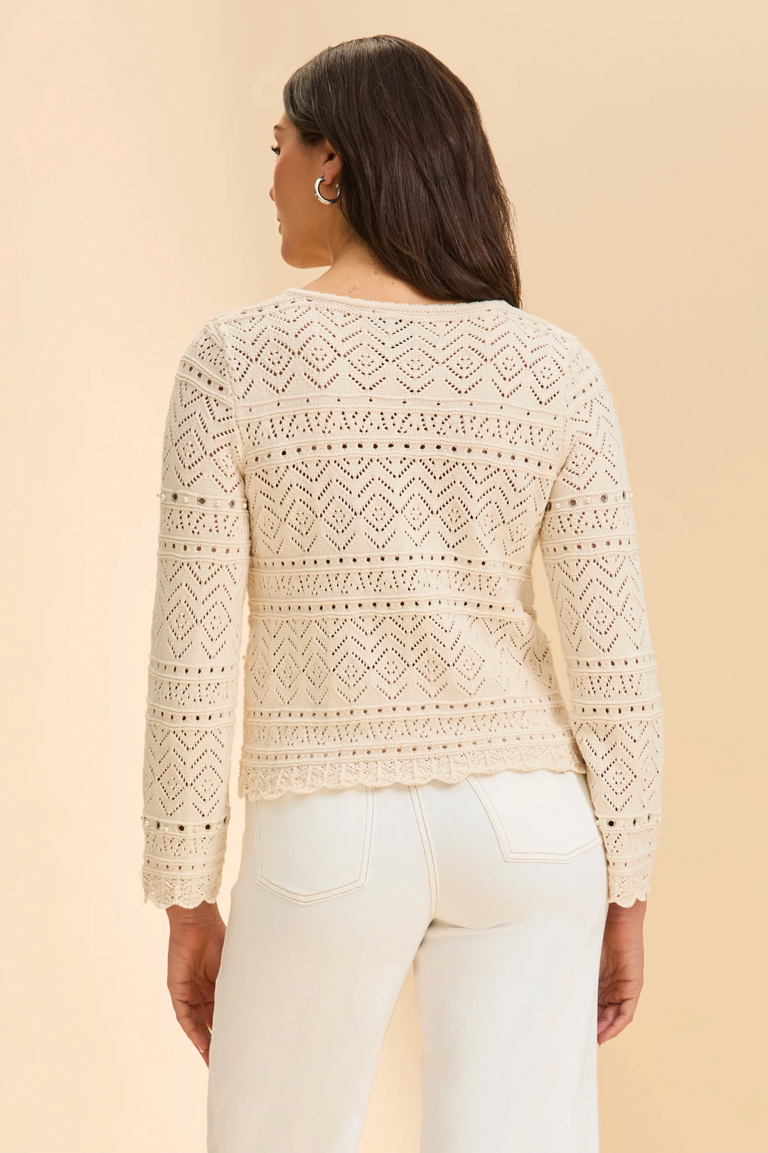 Woman wearing a cream lace top and white pants against a beige background