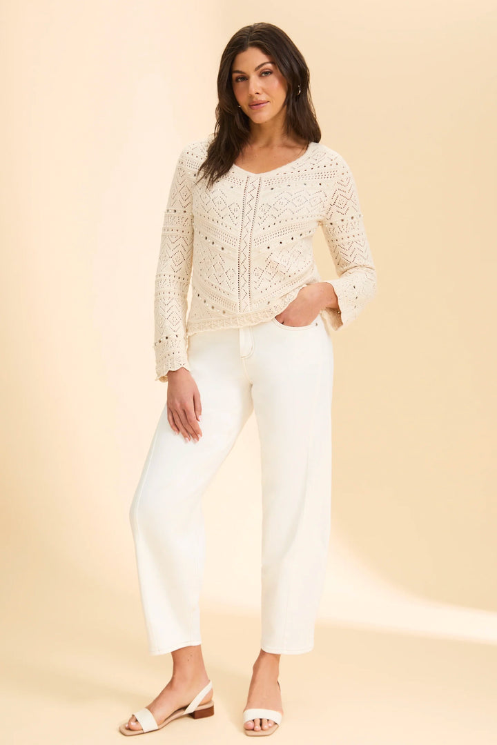 Woman wearing a cream lace top and white pants on a beige background