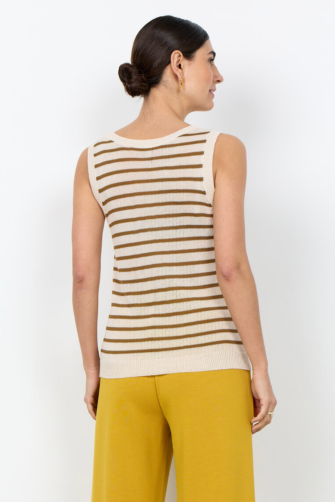 Woman wearing a stripe sleeveless top with yellow pants on a white background. 