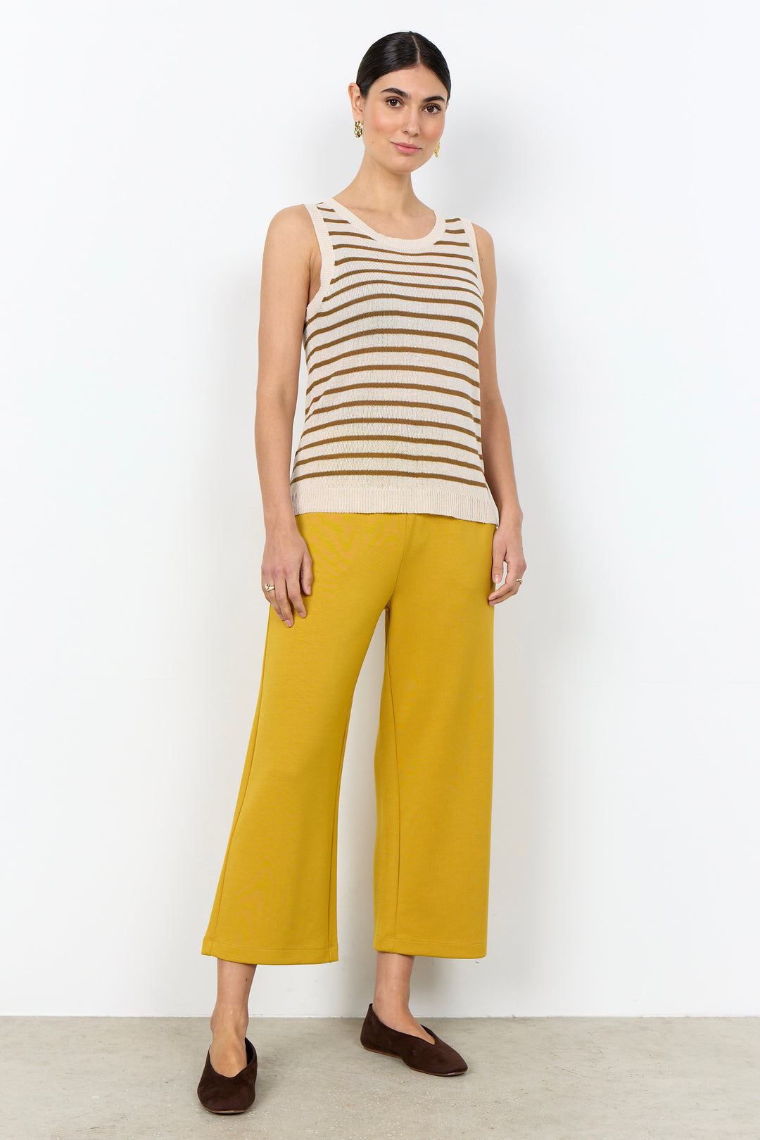 Woman wearing a stripe sleeveless top with yellow pants on a white background. 