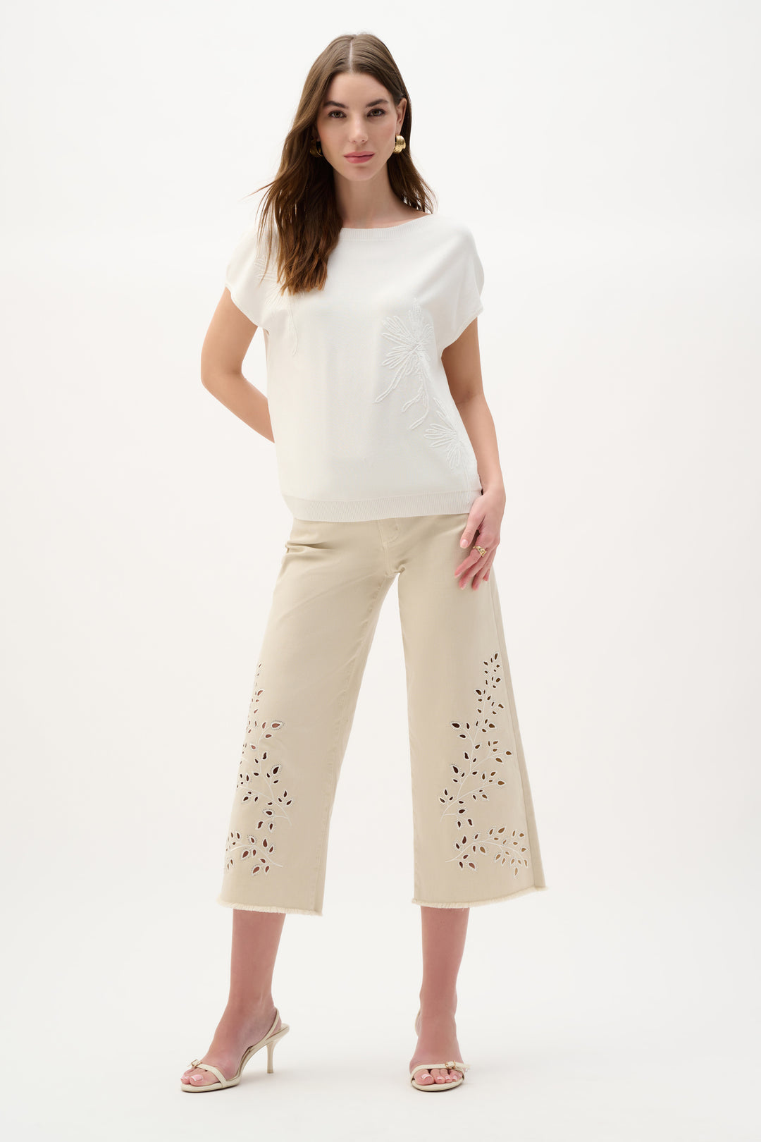 Woman wearing a white top and beige pants with embellishments on a white background