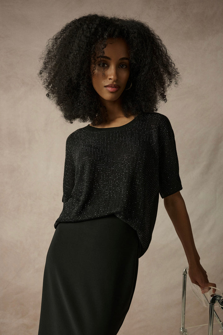 Woman wearing a black light metallic sweater against a beige background