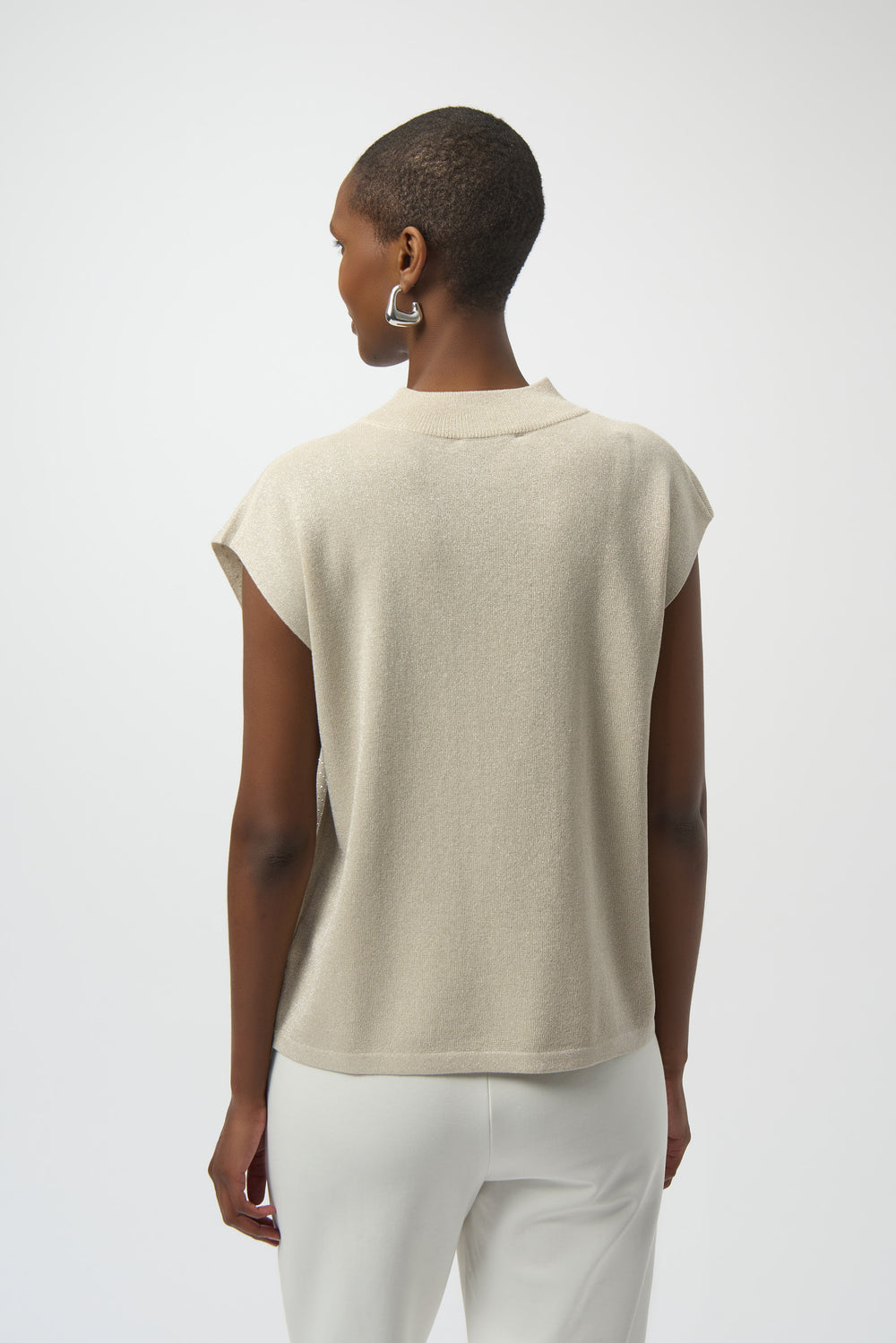 Person wearing a beige sleeveless top and white pants on a plain background