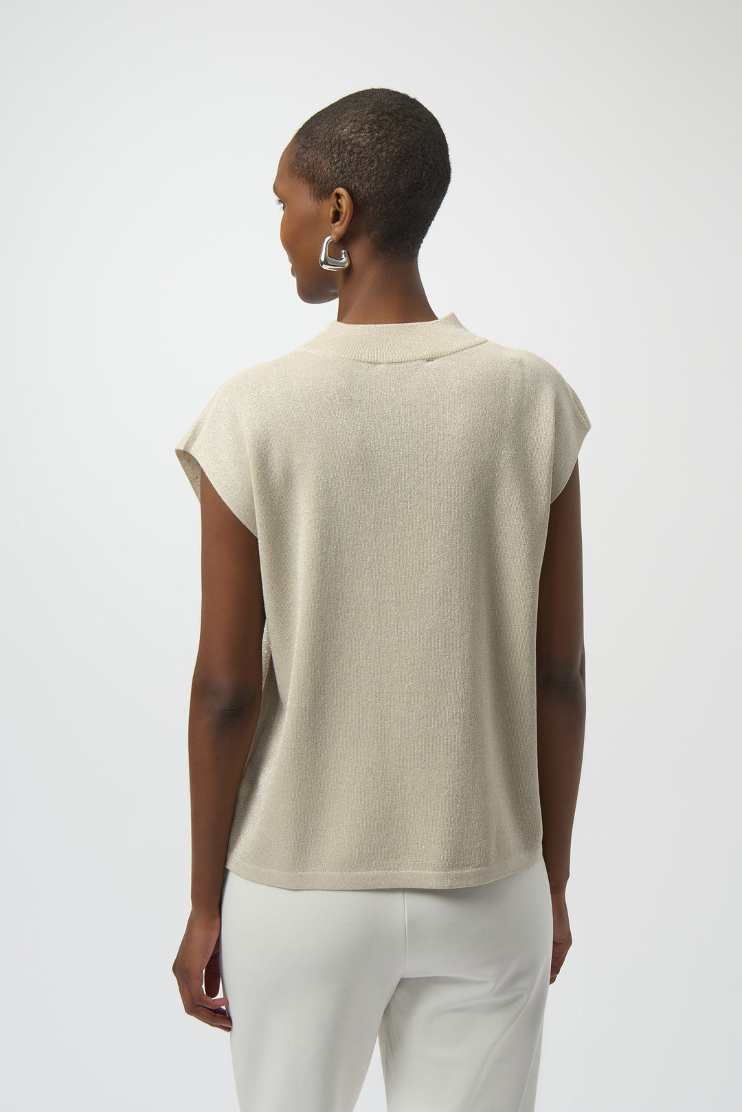 Person wearing a beige sleeveless top and white pants on a plain background
