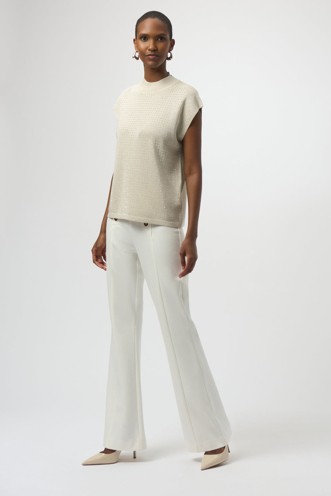 Woman wearing a beige sleeveless top and white pants on a white background