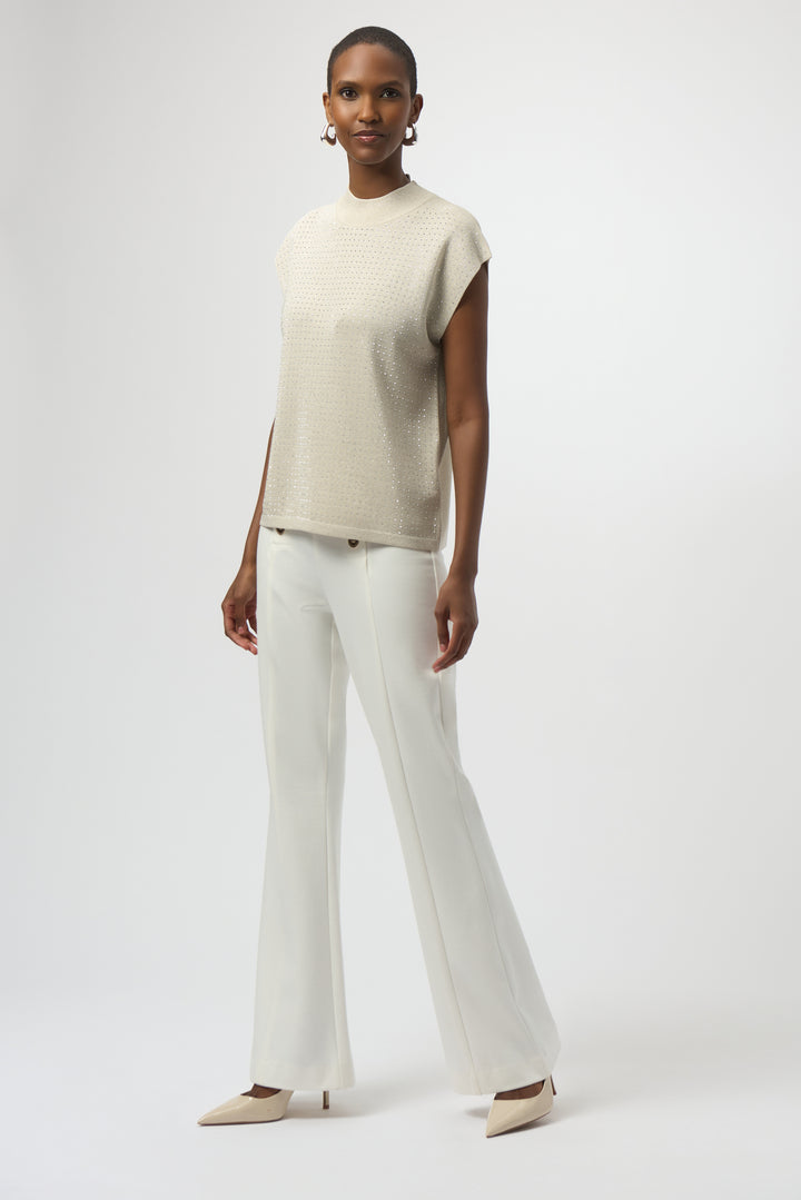 Woman wearing a beige sleeveless top and white pants on a white background