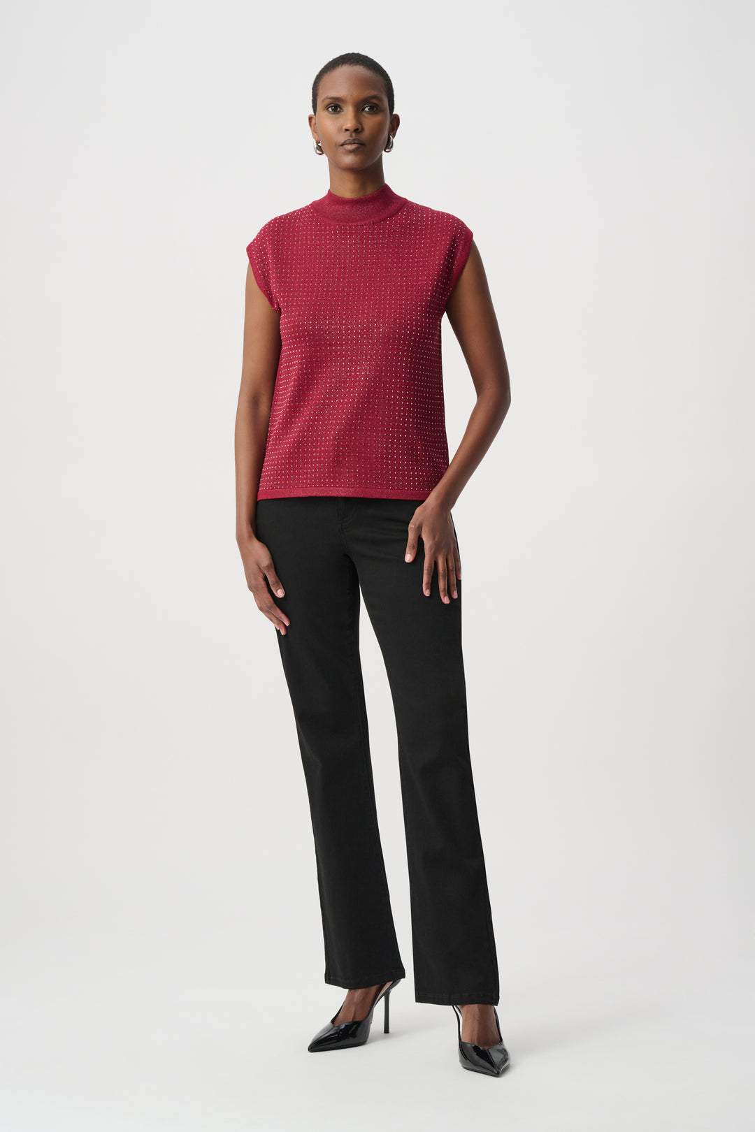Woman wearing a red sleeveless top with rhinestones and black pants on a white background