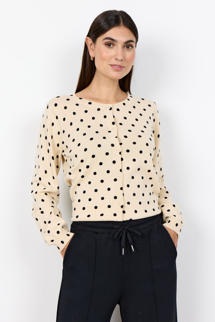 woman wearing a cream cardigan with black polka dots and black pants on a white background. 