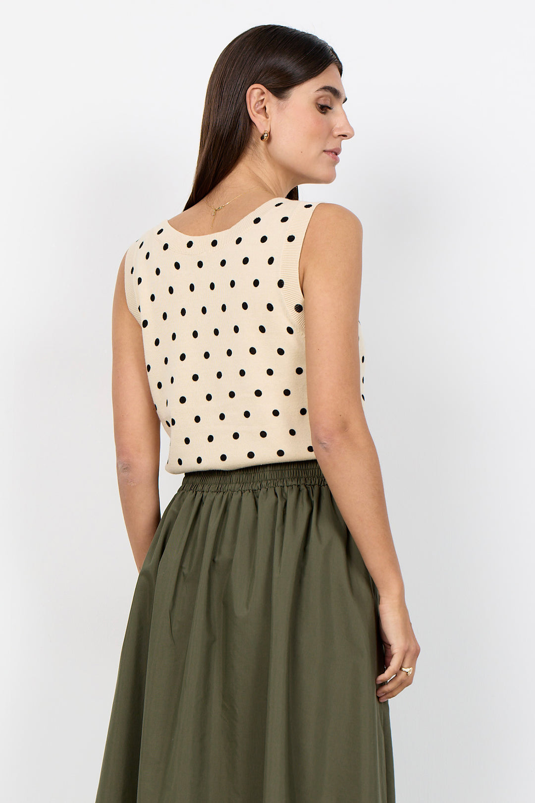 woman wearing a cream polka dot vest top and a khaki skirt on a white background.