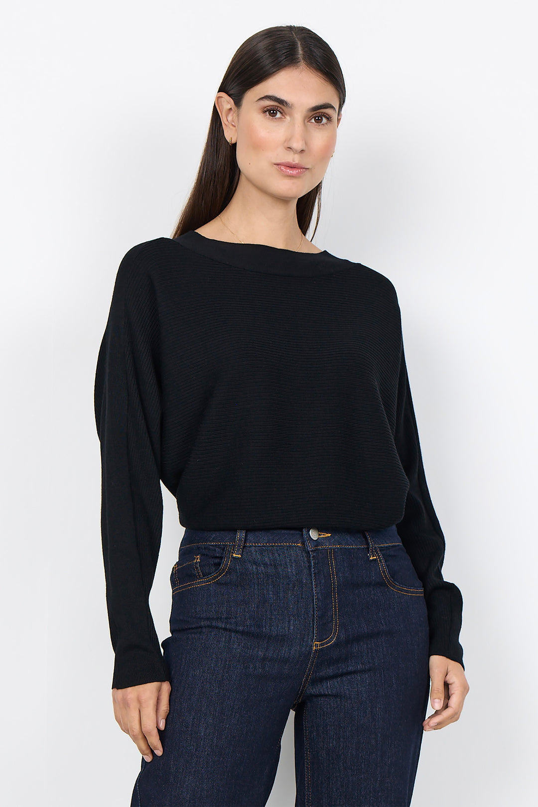 woman wearing a loose dolman sleeve sweater with jeans on a white background. 