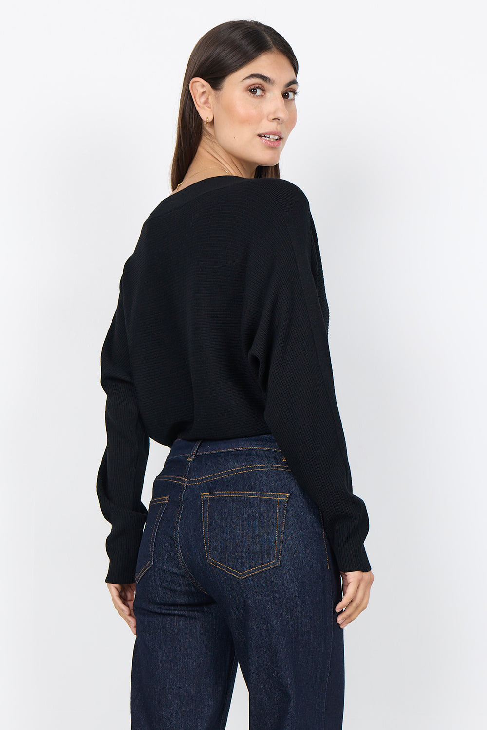 woman wearing a loose dolman sleeve sweater with jeans on a white background. 