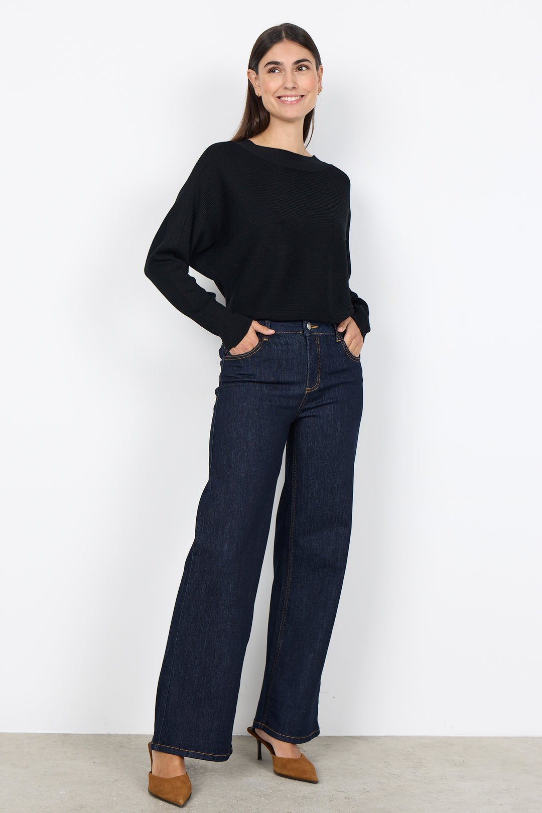 woman wearing a loose dolman sleeve sweater with jeans on a white background. 