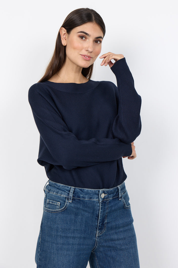 woman wearing a loose dolman sleeve sweater with jeans on a white background. 