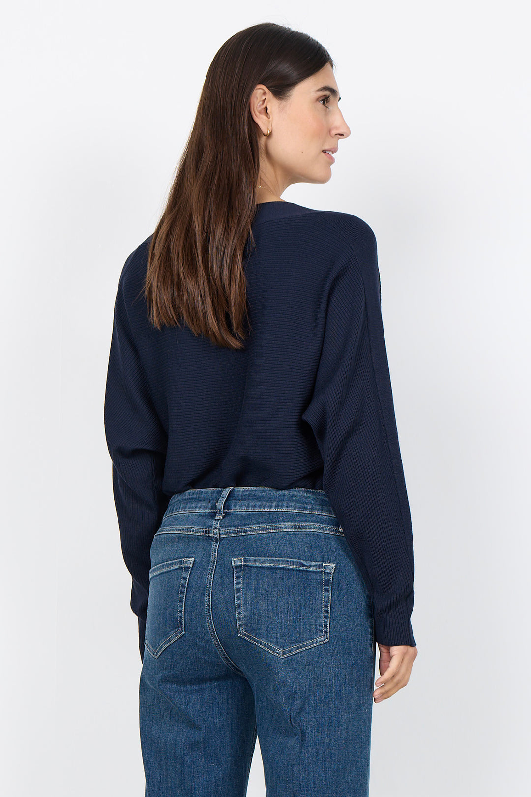 woman wearing a loose dolman sleeve sweater with jeans on a white background. 