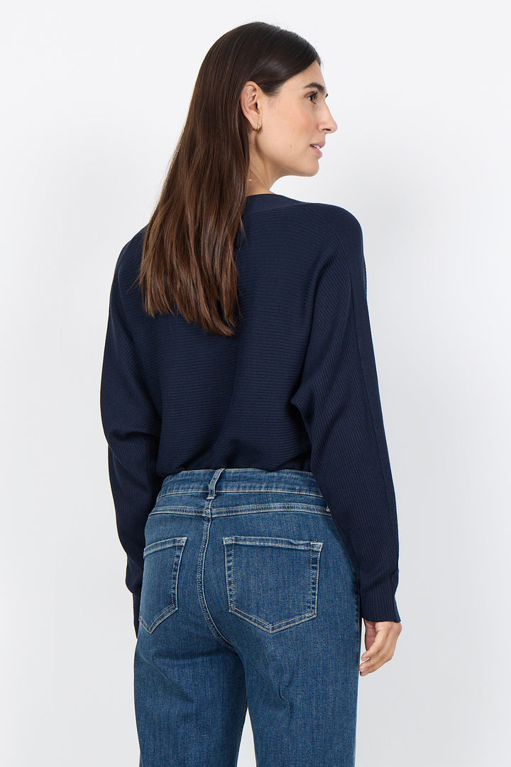 woman wearing a loose dolman sleeve sweater with jeans on a white background. 