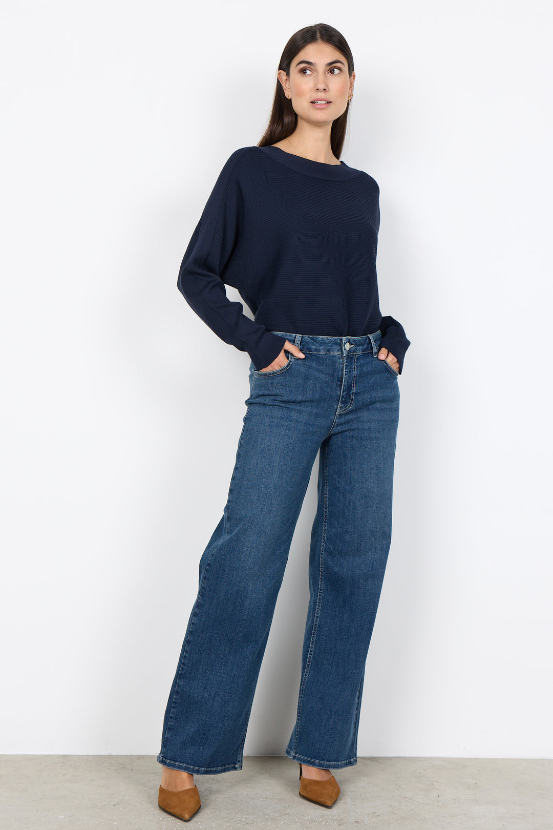 woman wearing a loose dolman sleeve sweater with jeans on a white background. 