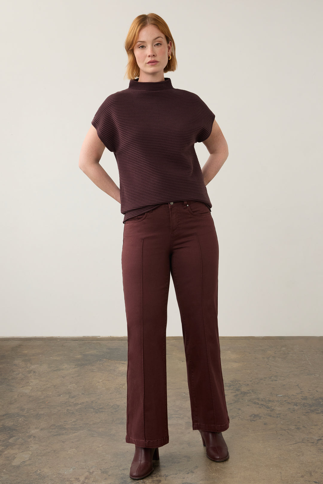 A woman modeling a dark burgundy ribbed short-sleeve mock neck top and matching wide-leg trousers against a neutral studio backdrop.