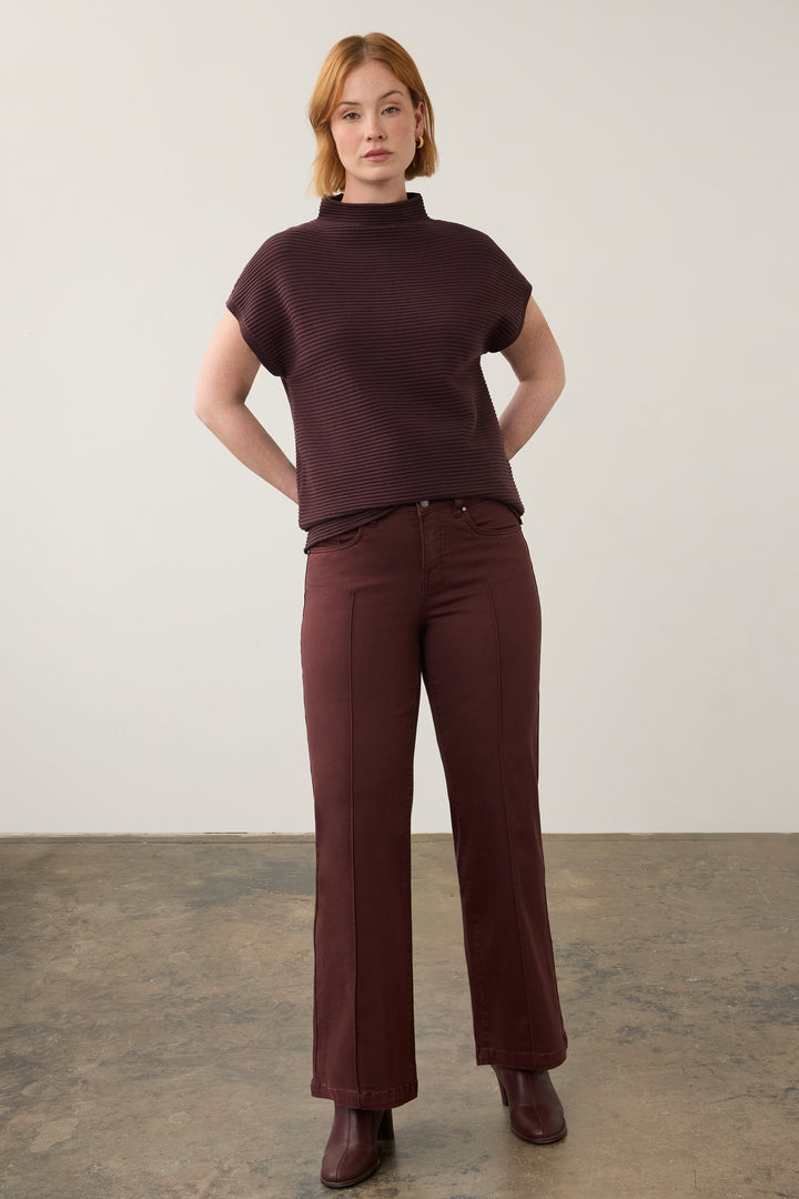 A woman modeling a dark burgundy ribbed short-sleeve mock neck top and matching wide-leg trousers against a neutral studio backdrop.