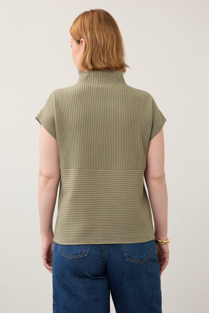 A woman viewed from the back wearing a ribbed short-sleeve mock neck top in olive green, paired with blue jeans, against a plain light background.