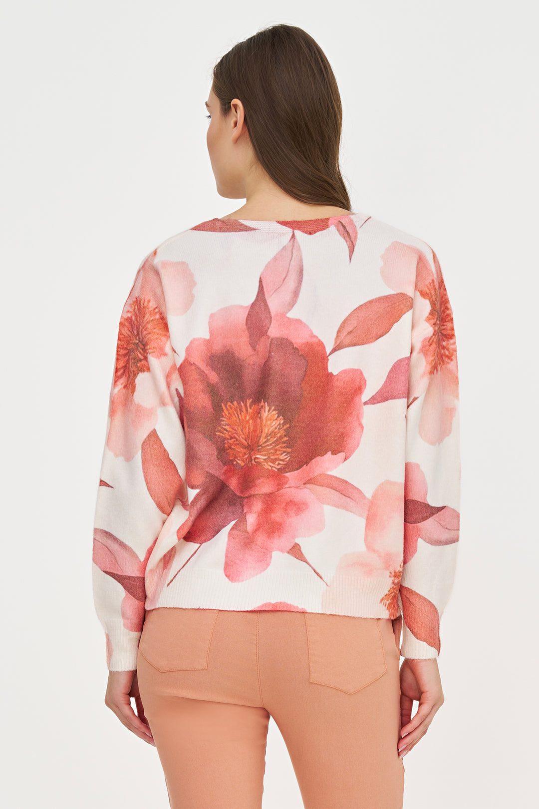 A woman shown from the back wearing a white long-sleeve top with a large pink and red floral print, paired with peach-colored pants, against a plain white background.