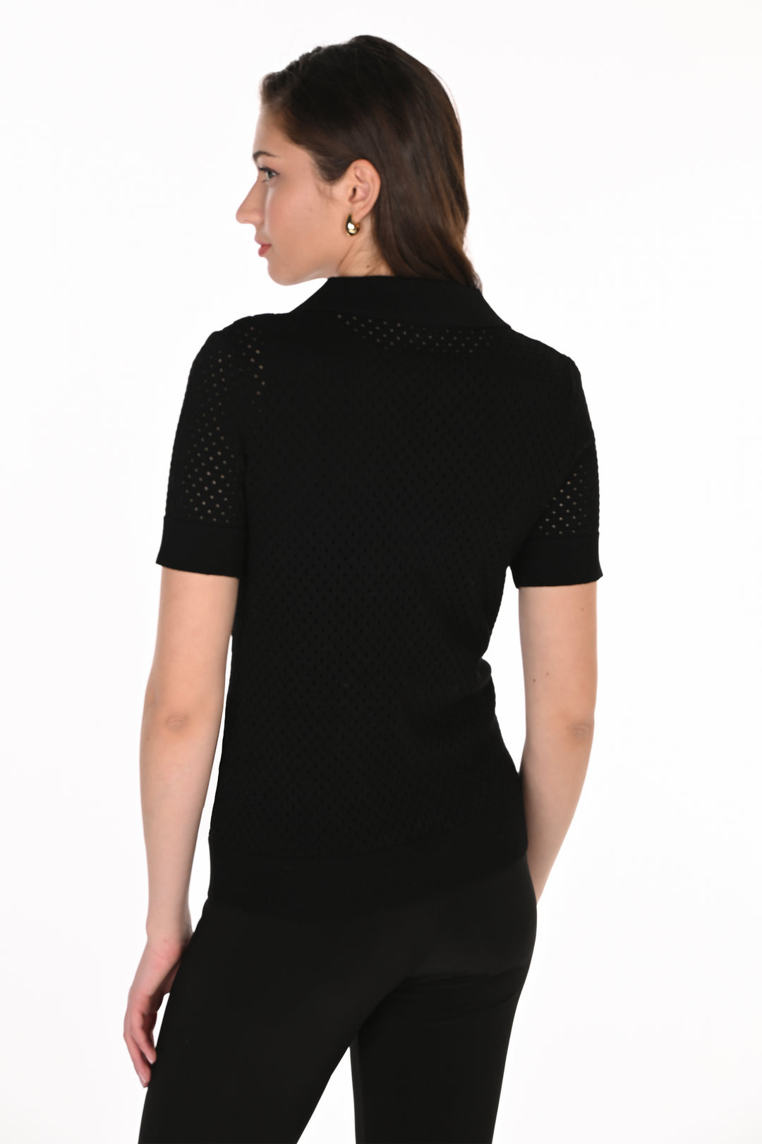 A woman shown from the back wearing a black short-sleeve knit top with textured openwork mesh detailing on the shoulders and upper back, paired with black pants, against a plain white background.