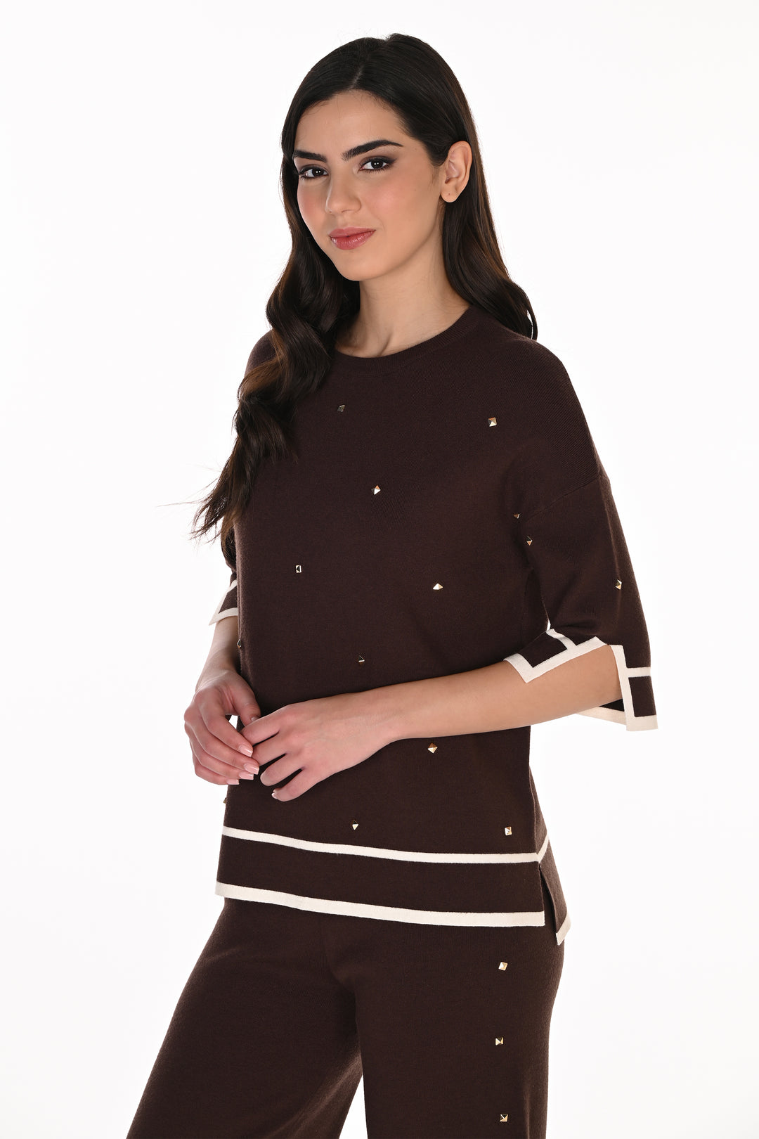 A woman modeling a dark brown knit top and matching pants set. The top features white contrast trim at the sleeve cuffs and hem, with small silver rhinestone embellishments scattered across the front.