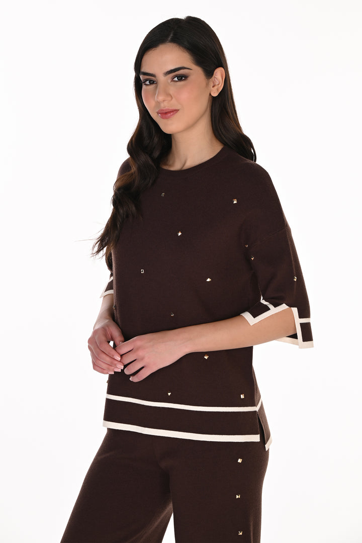 A woman modeling a dark brown knit top and matching pants set. The top features white contrast trim at the sleeve cuffs and hem, with small silver rhinestone embellishments scattered across the front.