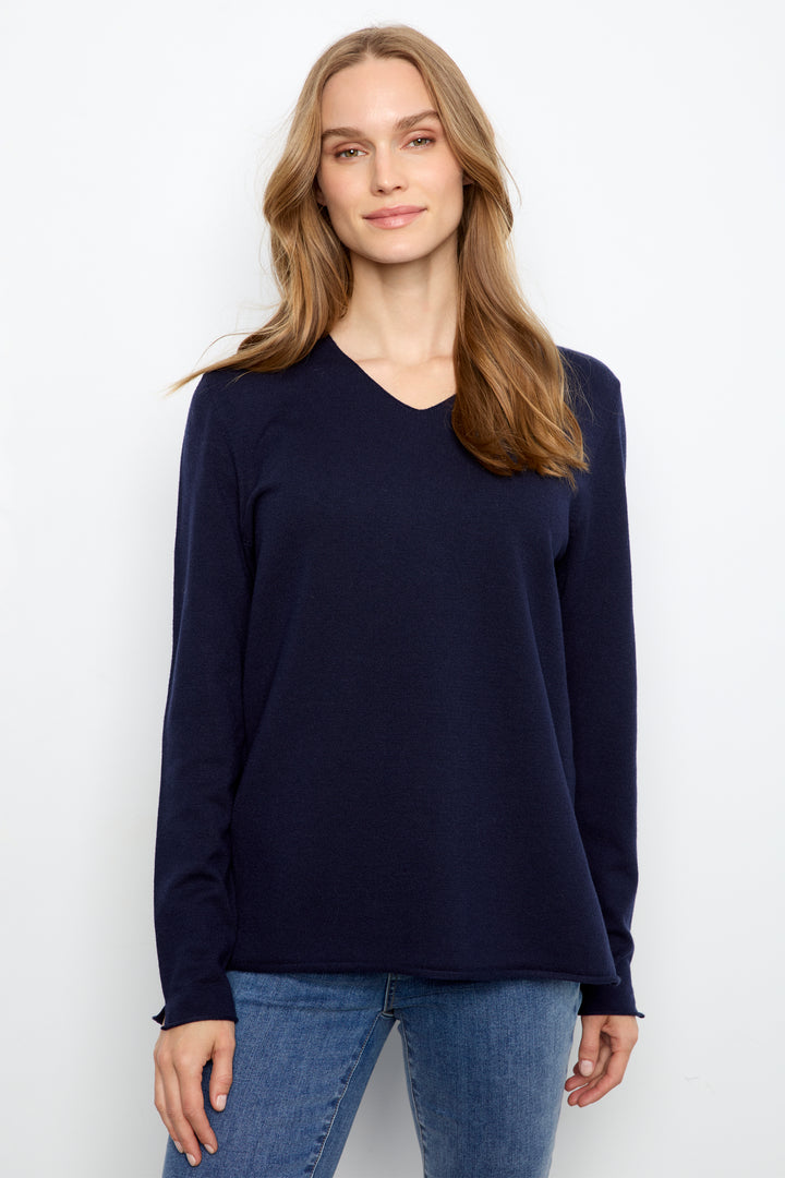 A woman wearing a dark navy blue long-sleeve V-neck sweater and blue jeans, standing against a plain white studio background.
