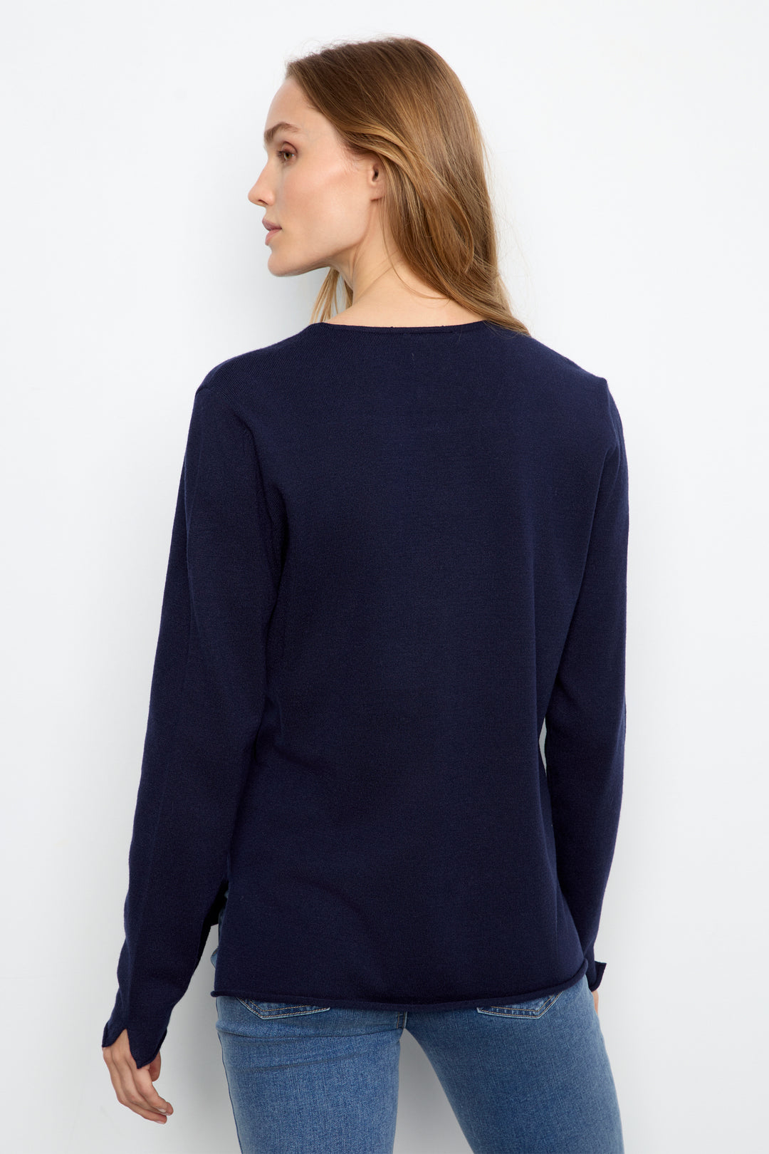 A woman shown from the back wearing a navy blue long-sleeve knit top and blue jeans against a plain white studio background.