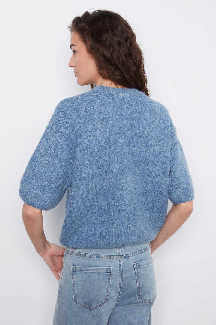 A woman shown from the back wearing a textured, short-sleeved knit top in a heathered medium blue color, paired with light-wash jeans, against a plain white background.