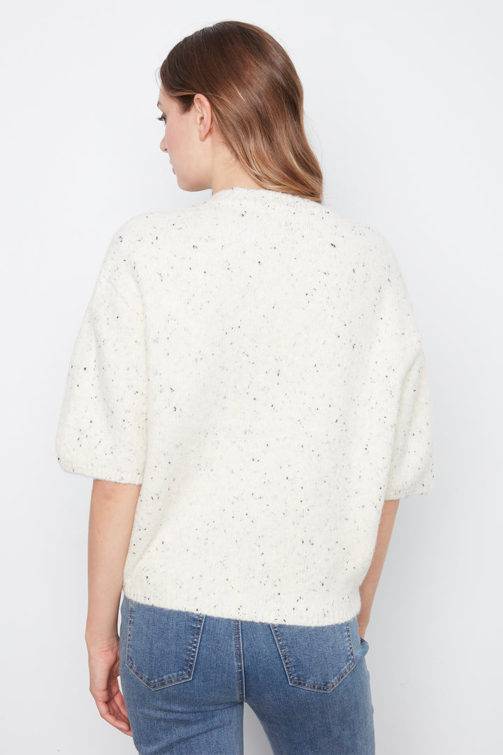 A woman shown from the back wearing a textured cream knit top with small dark speckles and blue jeans, against a plain white studio background.