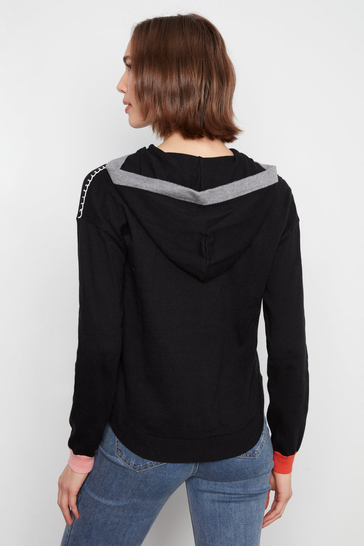 A woman shown from the back wearing a black hoodie with a gray chevron pattern across the shoulders and silver chain detailing on the sleeve, paired with blue jeans against a plain white background.