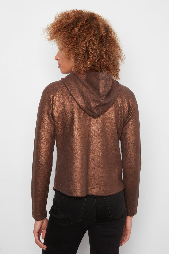 A person shown from the back wearing a metallic bronze cropped hoodie with black pants, photographed against a plain light gray studio background.