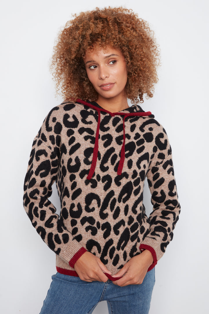 A woman with curly brown hair wearing a beige and black leopard print knit hoodie with dark red drawstrings and cuffs, paired with blue jeans, against a plain white background.